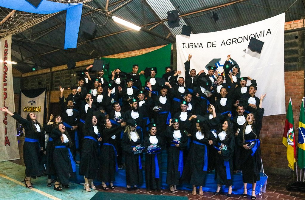 fotografia colorida mostra uma turma de formandos usando beca e com diploma na mão comemora a conquista da formação
