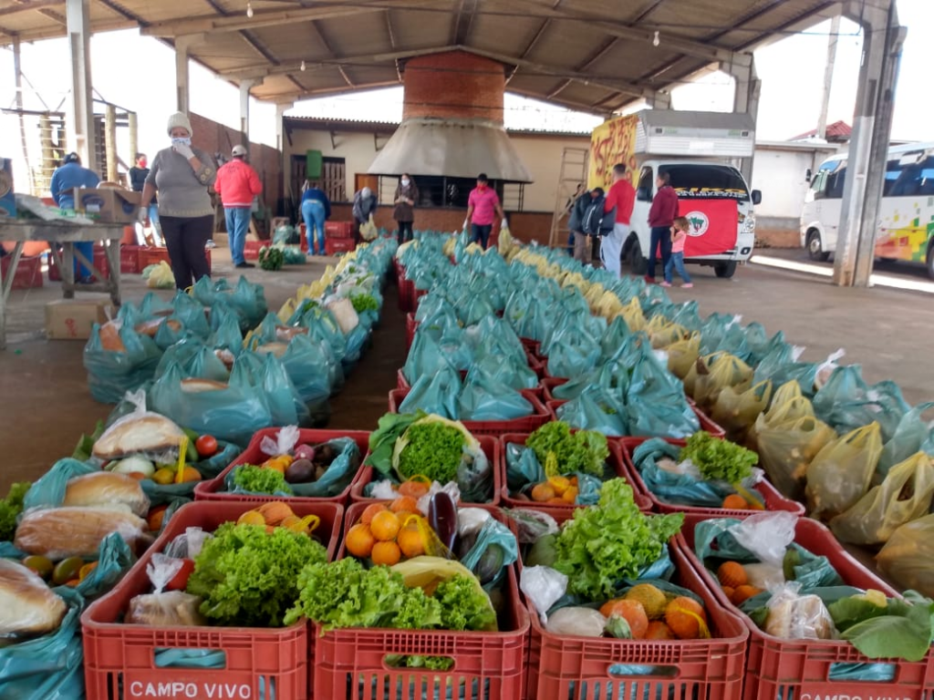 fotografia colorida mostra uma galpão pré-moldado onde estão dispostas centenas de caixas e sacolas com alimentos para doação