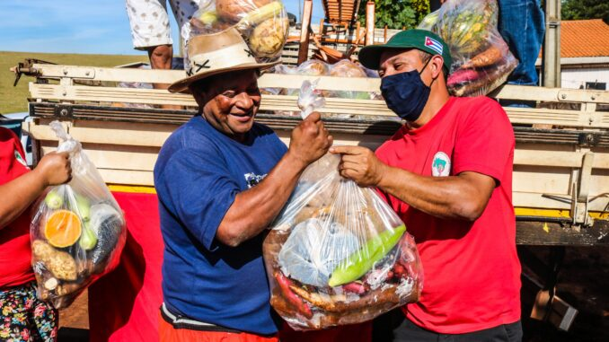 fotografia colorida mostra dois homens segurando uma sacola de alimentos provavelmente um entregando a comida ao outro